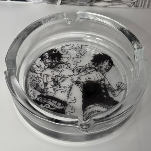 The Ace Luffy Ashtray by SpicedAnime is a clear glass ashtray decorated inside with black-and-white manga-style art of two muscular characters, one wreathed in smoke—a bold anime-themed collectible.