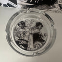 The SpicedAnime Ace Luffy Ashtray showcases striking black and white art of two characters in battle, displayed on a white surface with manga pages peeking through in the background.